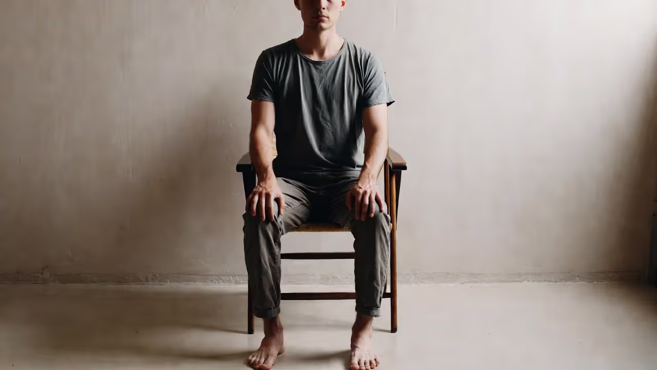 Person sitting in a chair with feet flat on the floor and hands pressing on thighs.