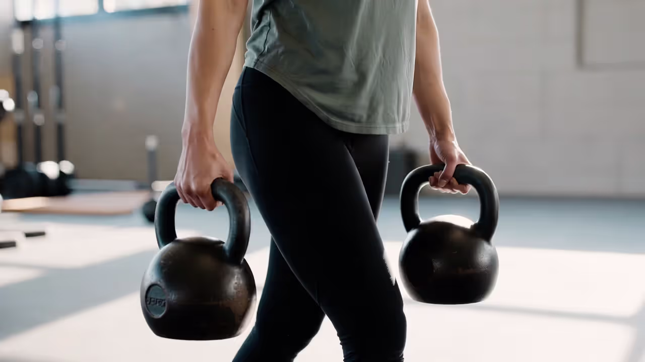Person performing a farmer carry while maintaining upright posture and core stability.