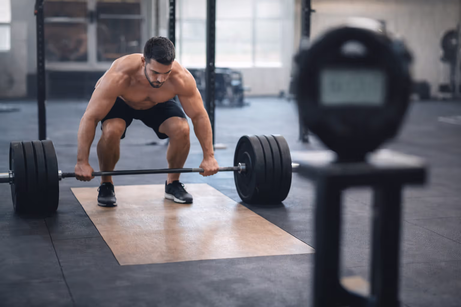 Powerlifter preparing for a heavy single rep with a blurred timer nearby