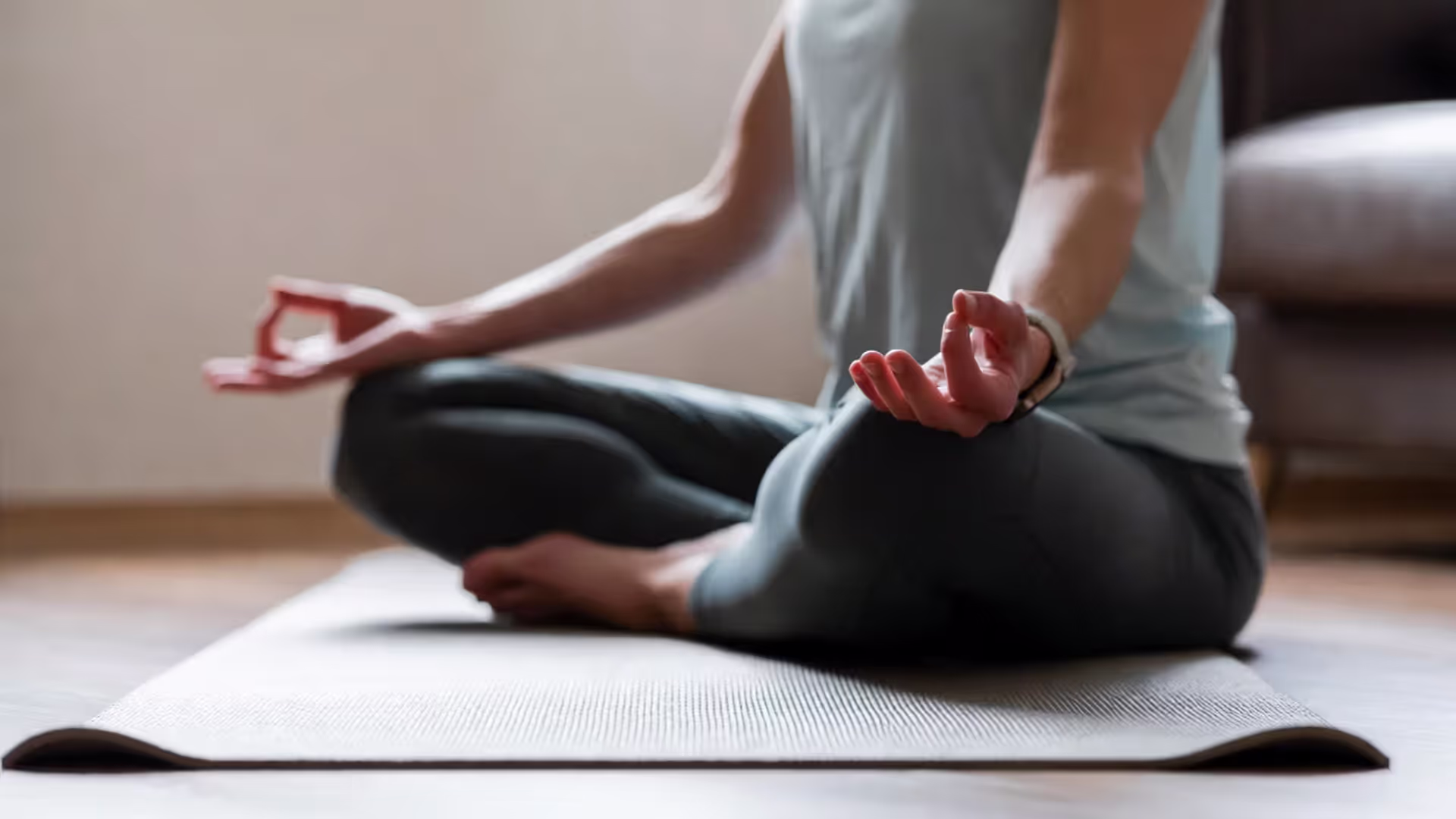 Person seated cross-legged on a yoga mat with eyes closed, preparing for breathing practice, wearing a heart-rate watch.