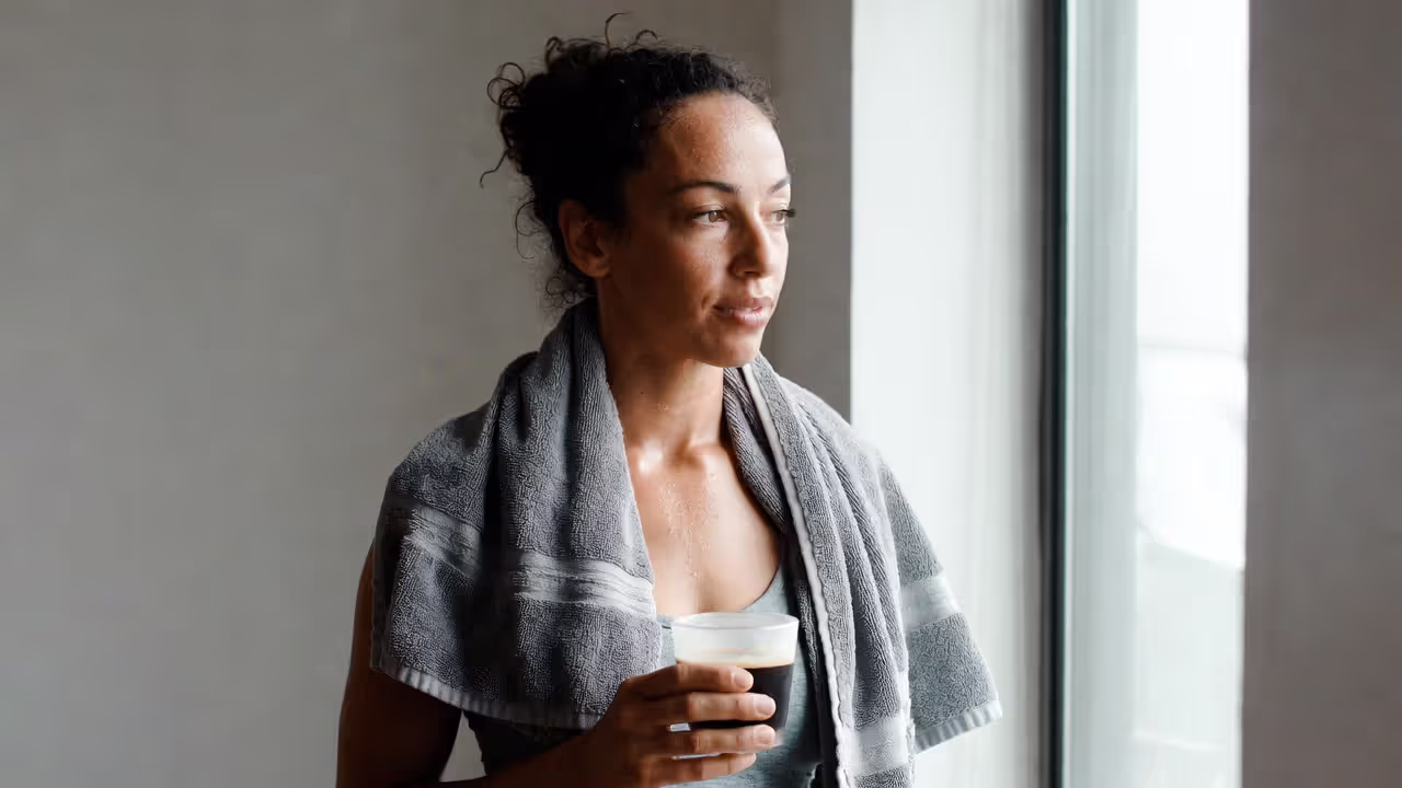 Person standing by a window after a morning workout, looking focused and calm