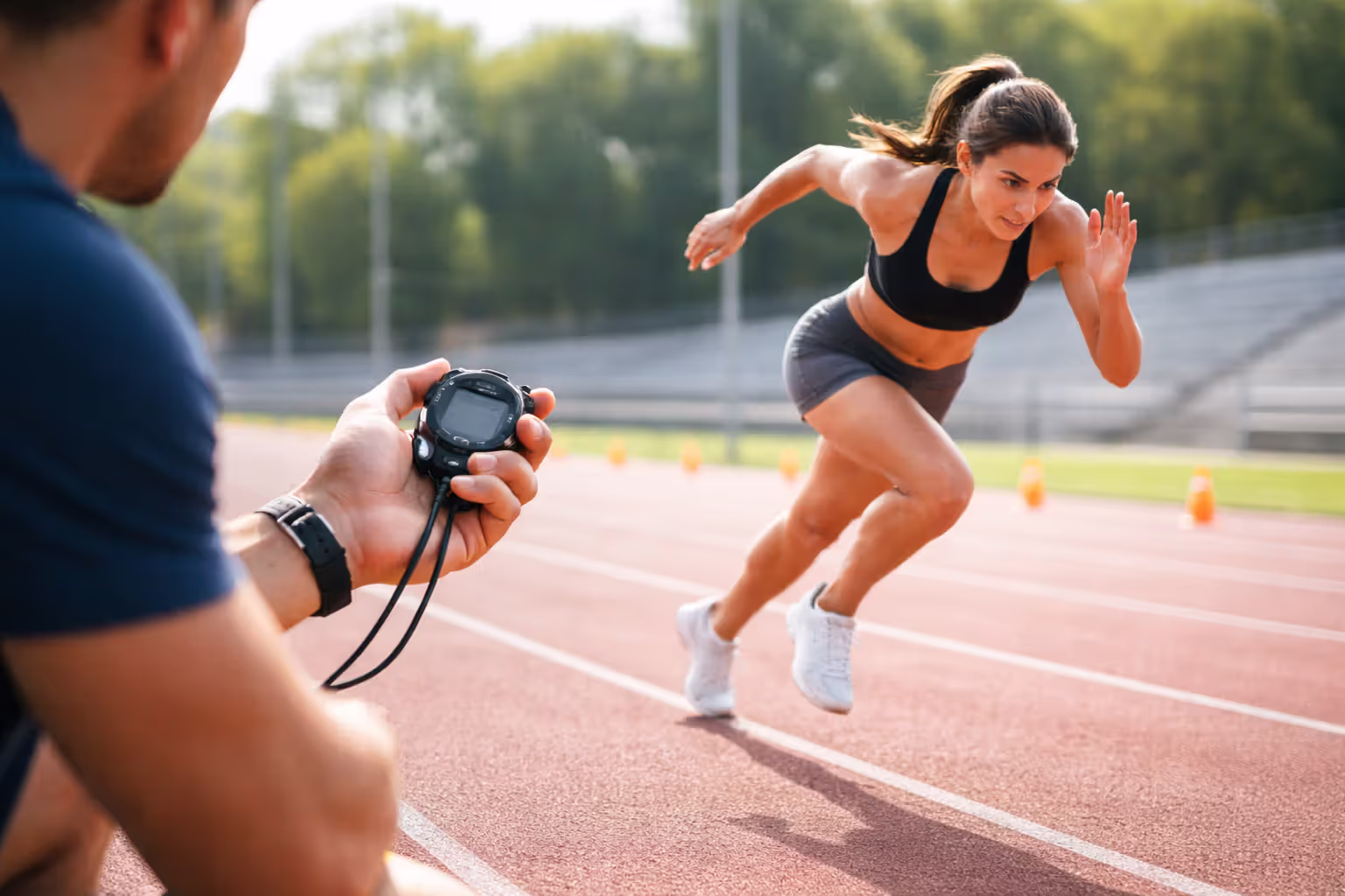 Athlete sprinting on a track while a coach times the interval